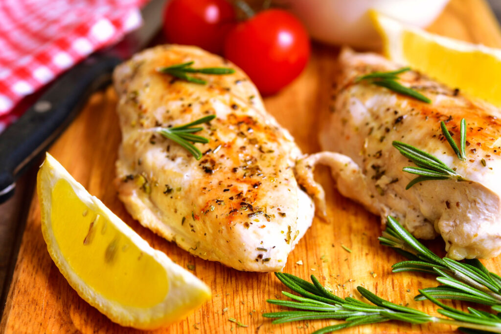 Cooked chicken with spices and rosemary sitting on a cutting board.