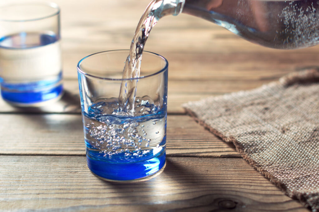 Clear pitcher pouring water into clear glasses on a wooden table.