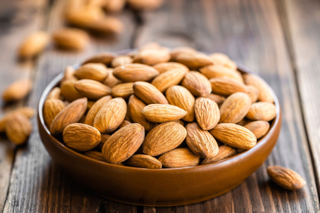 Almonds top off a brown bowl placed on a wooden table.