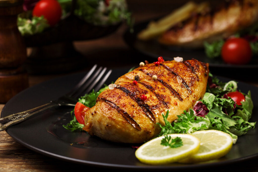 Black plate with grilled chicken and salad greens and lemon slices.