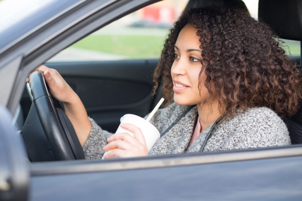 Woman driving while holding a white cup with a straw.