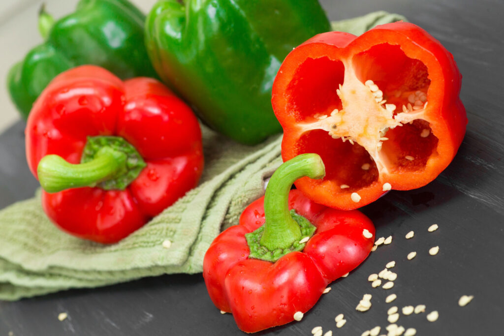 Green and red bell peppers with a red bell pepper cut open and seeds spilling out.