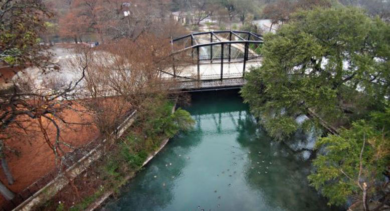 Bird’s eye view of bridge and river flowing through Brackenridge Park in San Antonio.