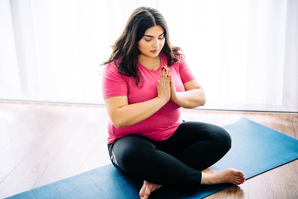 Plus-size woman doing yoga to learn how to reduce abdominal fat.