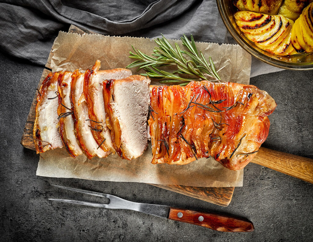 Slices of pork on parchment next to rosemary as an example of one of the healthy meats to eat.