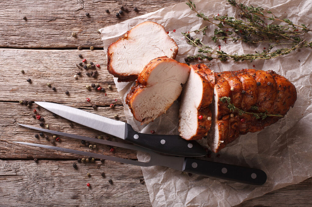 Turkey cut into slices on parchment next to knife.