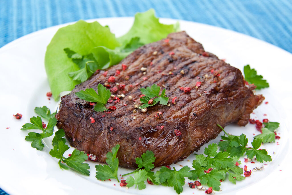 Slab of buffalo sprinkled with herbs on a white plate.