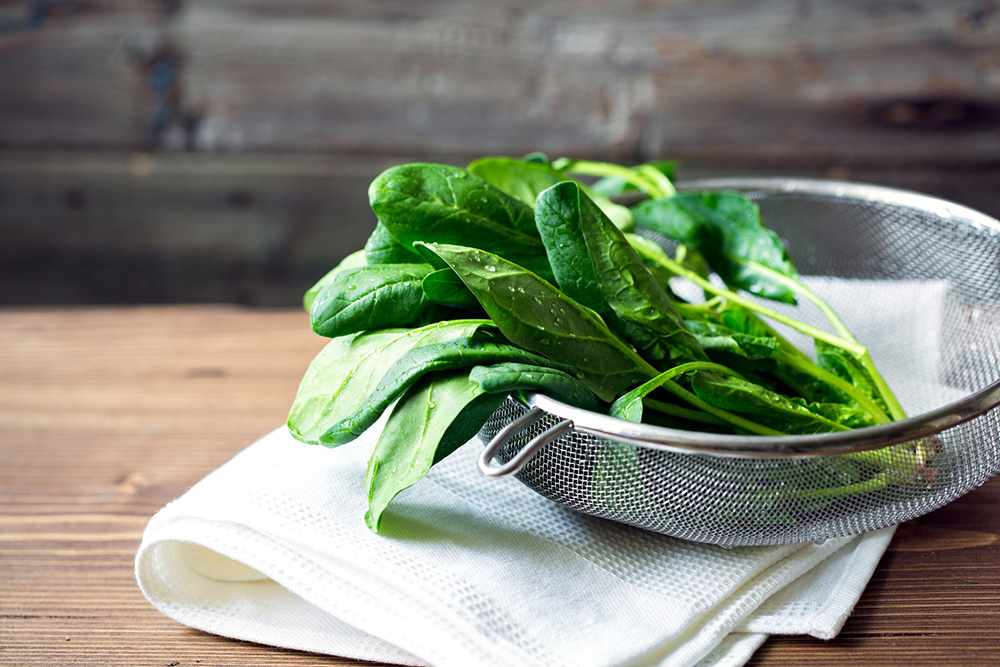 Drainer with wet spinach sitting on top of a white cloth.