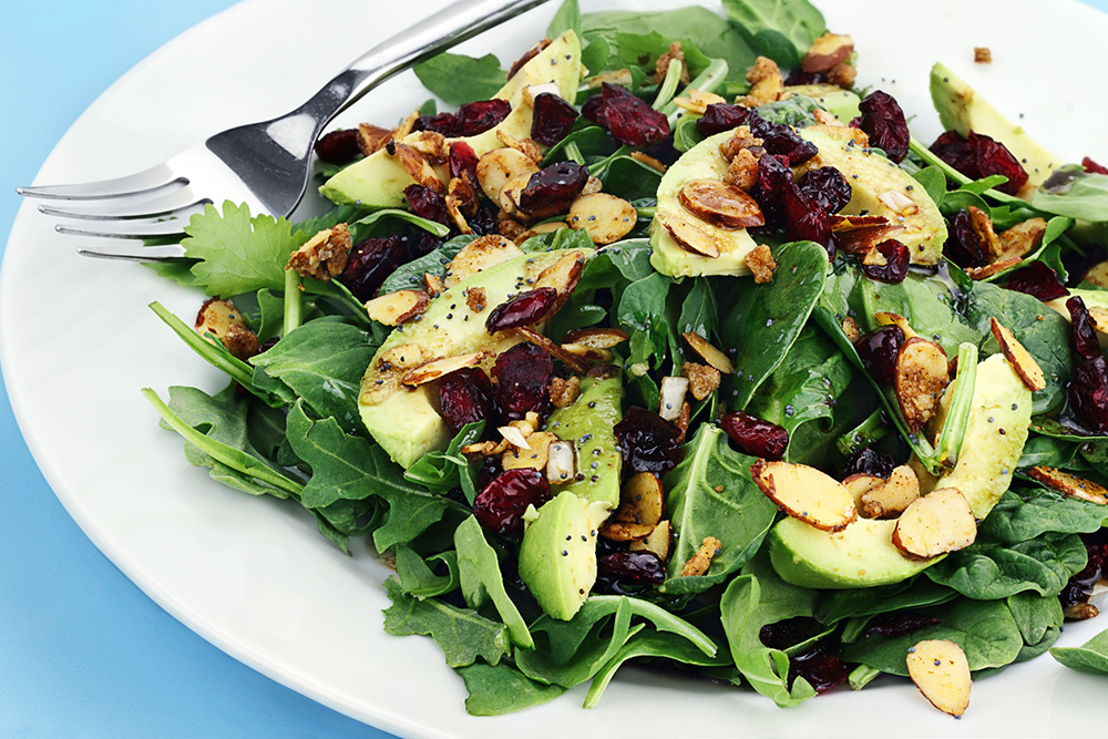 Close-up of a white salad bowl with spinach, avocado and nuts.