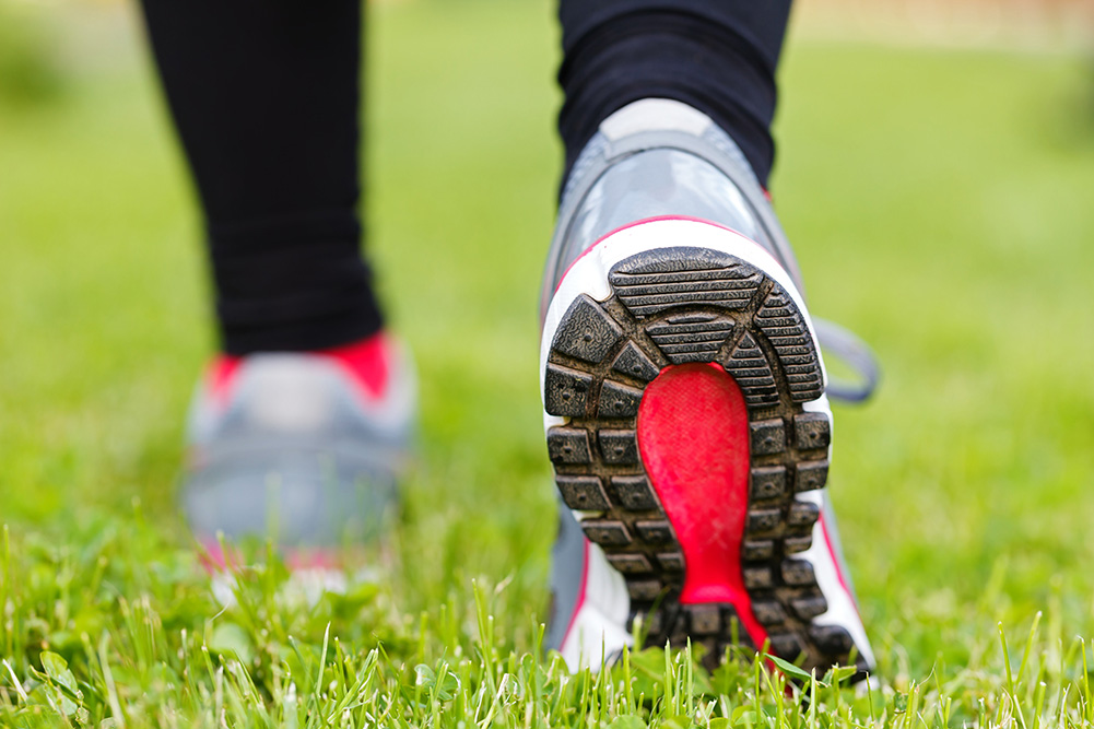 A close-up of a woman’s tennis shoes as she walks through grass.