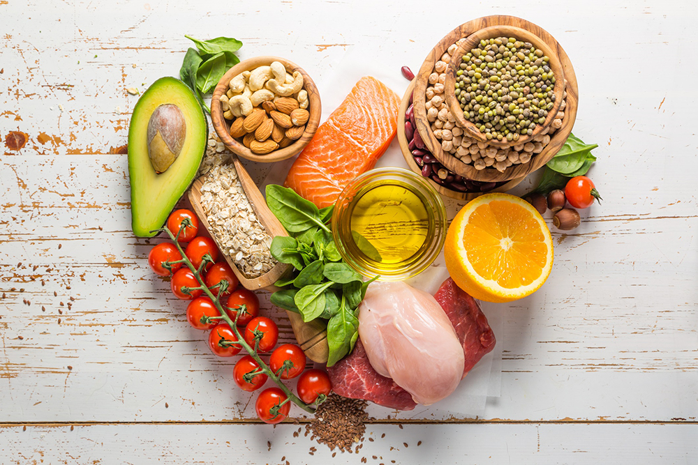 Nuts, salmon, meats, avocado, tomatoes gathered in the shape of a heart.