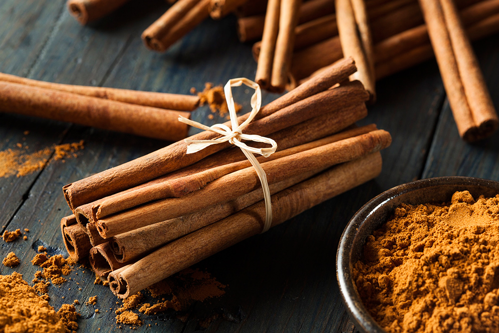 A bundle of cinnamon sticks tied up near a bowl of cinnamon powder.