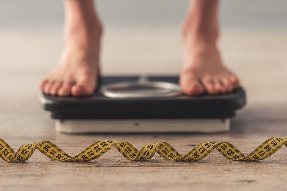 Measuring type on the ground in front of a person standing on a scale to represent the health benefits of walking.