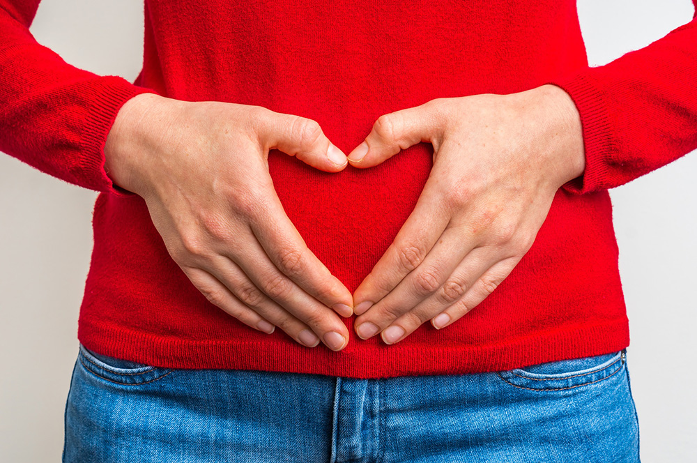 Close-up of person making shape of heart with hands around abdomen area.